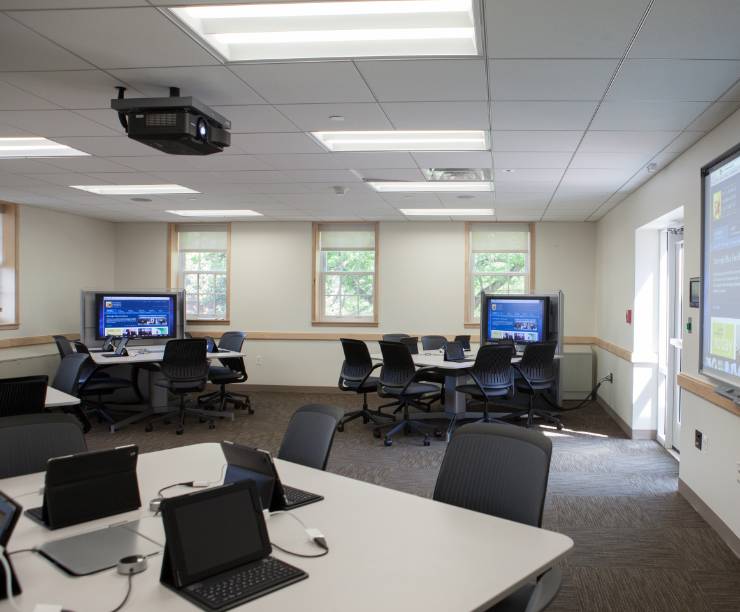 An empty classroom with laptop computers on a table, a smart board, and projector.