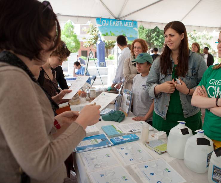 Four women standing behind a table while assisting visitors at GW?s Sustainability Fair.