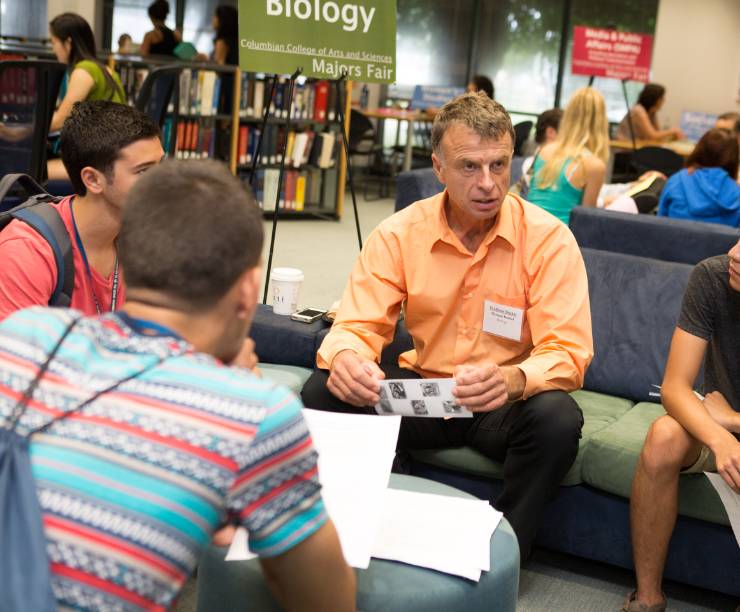 Professor is seated in the library talking informally with several students