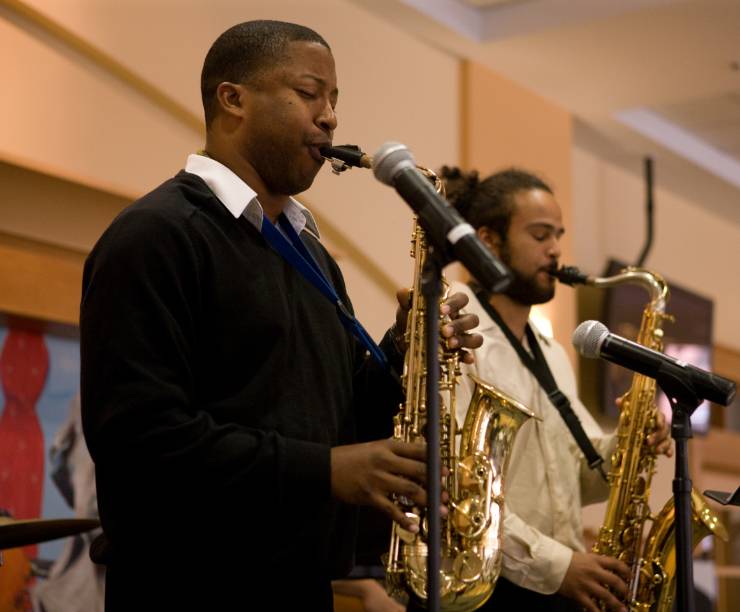 Two men play saxophones in front of microphones.