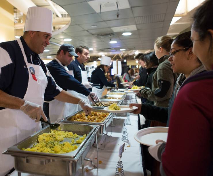 Faculty members serve hot food to a line of students.