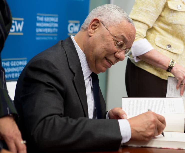 General Colin Powell sits at a table signing a book.