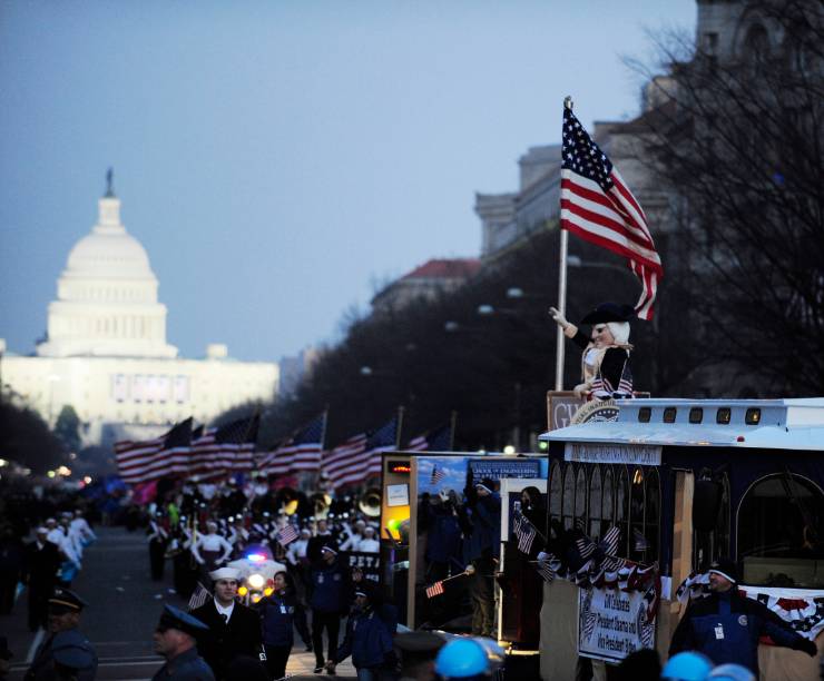 A float with the George Mascot and American flag drives through a parade crowd with the Capitol in the background.