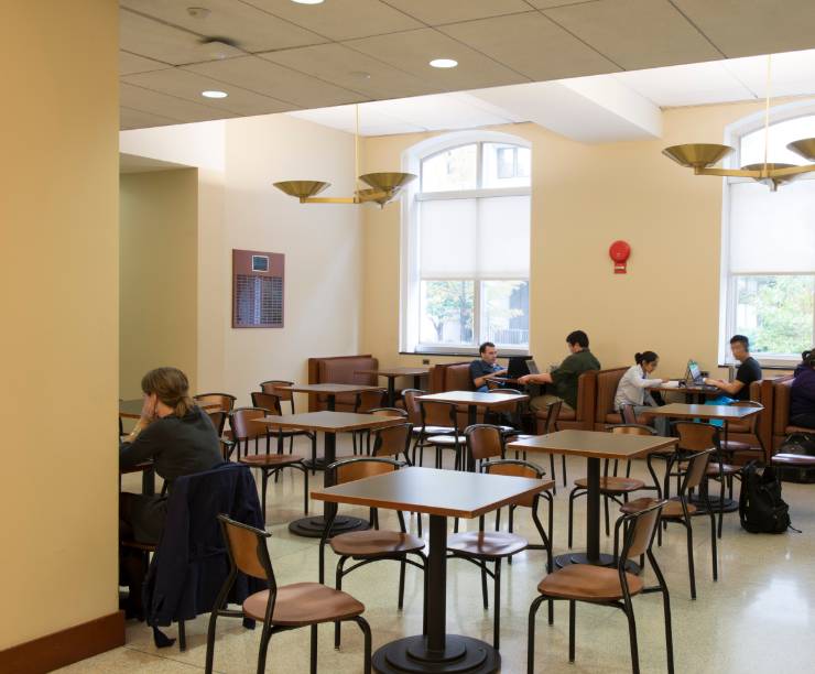 Students studying and hanging out in GW Law's ?hard? lounge at hard surface dining tables and chairs and a number of benches.