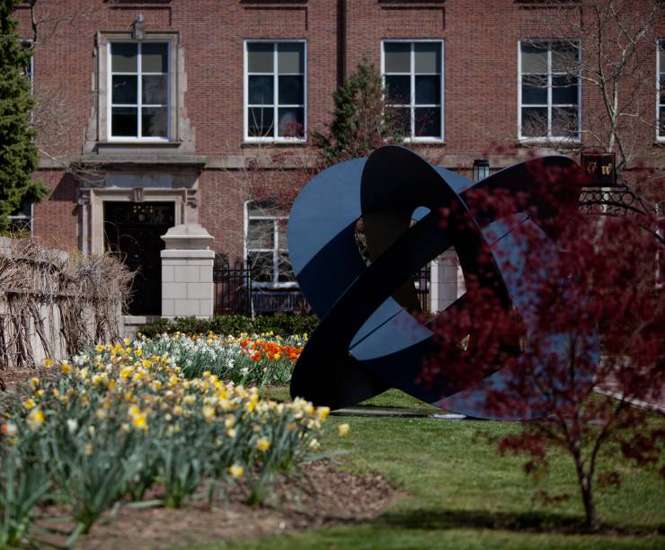 A black steel and bronze sculpture and blooming daffodils brighten the Quad.