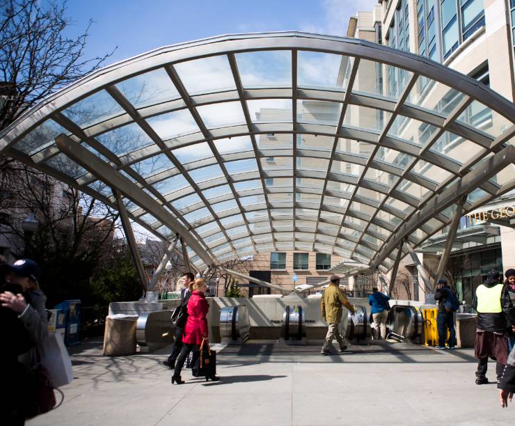 The glass and steel metro entrance with people walking by.