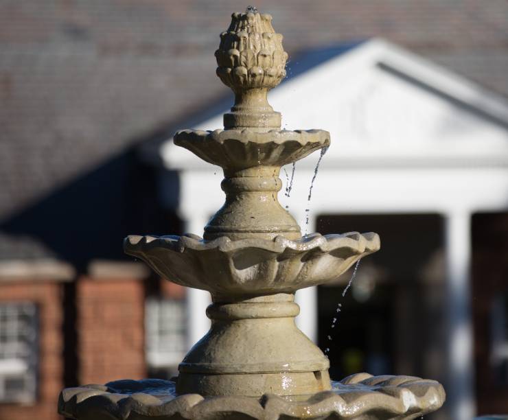 The three-tiered fountain sits before a red-brick hall.