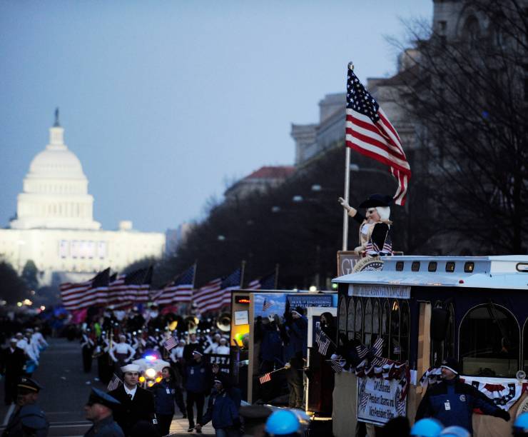 A float with the George Mascot and American flag drives through a parade crowd toward the Capitol.