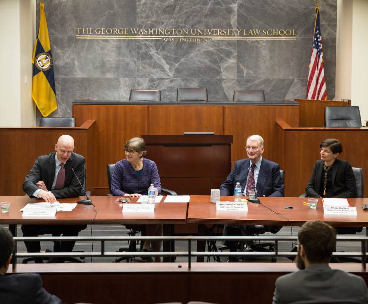 Four members of a panel have a discussion in front of an audience in the Jacob Burns Moot Court Room.