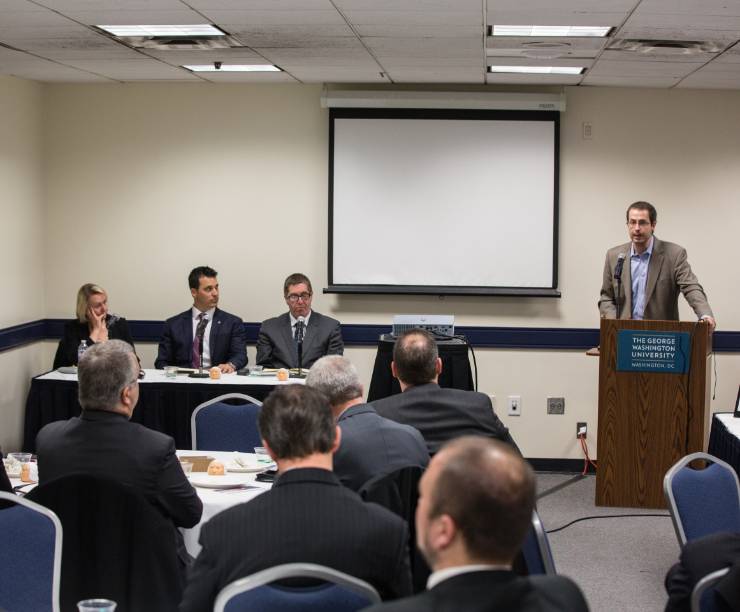 Three speakers and a moderator sit at the front of a classroom.