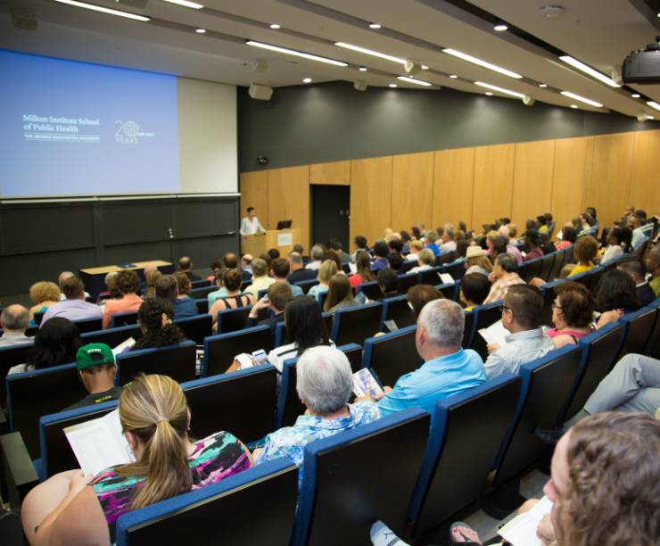 Large auditorium filled with an audience, and a speaker on stage behind a podium.