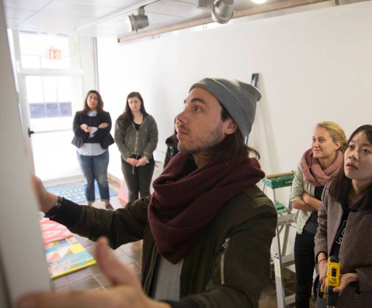 Students gather together and look at a man hanging a picture on a wall.