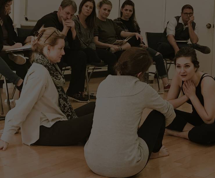 Two students sit on the floor with actor Laura Linney, and other students sit in chairs looking on.