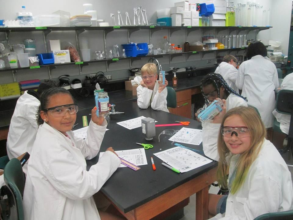 Kids in lab coats and safety goggles around a table in the lab at the BTCI.