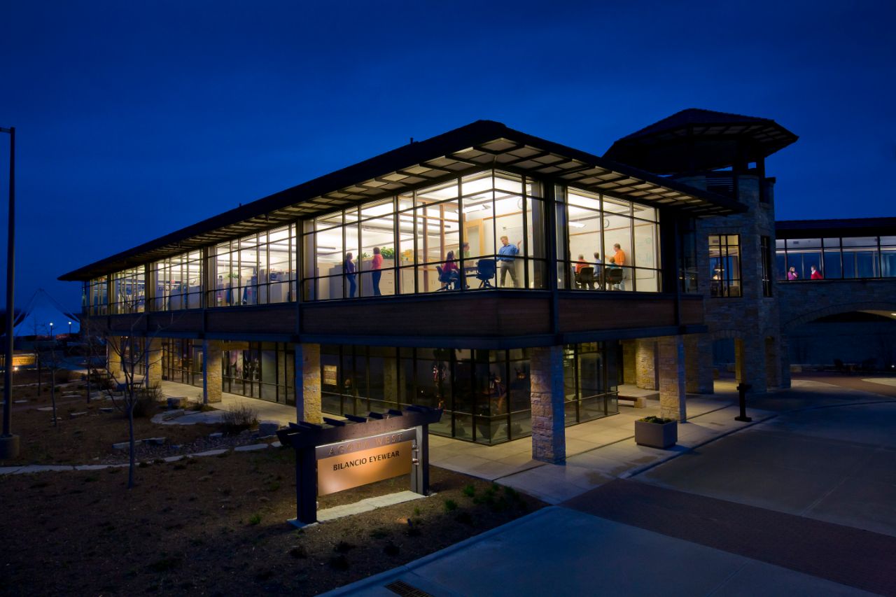 The Agora building at night, with lights shining on the Agora sign and a meeting happening on the second floor.