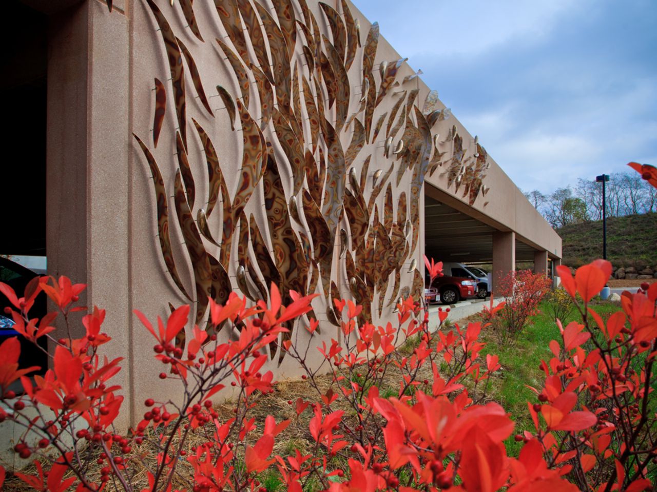 This photo shows the pieces of art on the outside of the Feynman parking ramp that are made of metal and adhered to the structure, along with red wild flowers in the foreground.