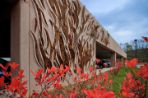 This photo shows the pieces of art on the outside of the Feynman parking ramp that are made of metal and adhered to the structure, along with red wild flowers in the foreground.