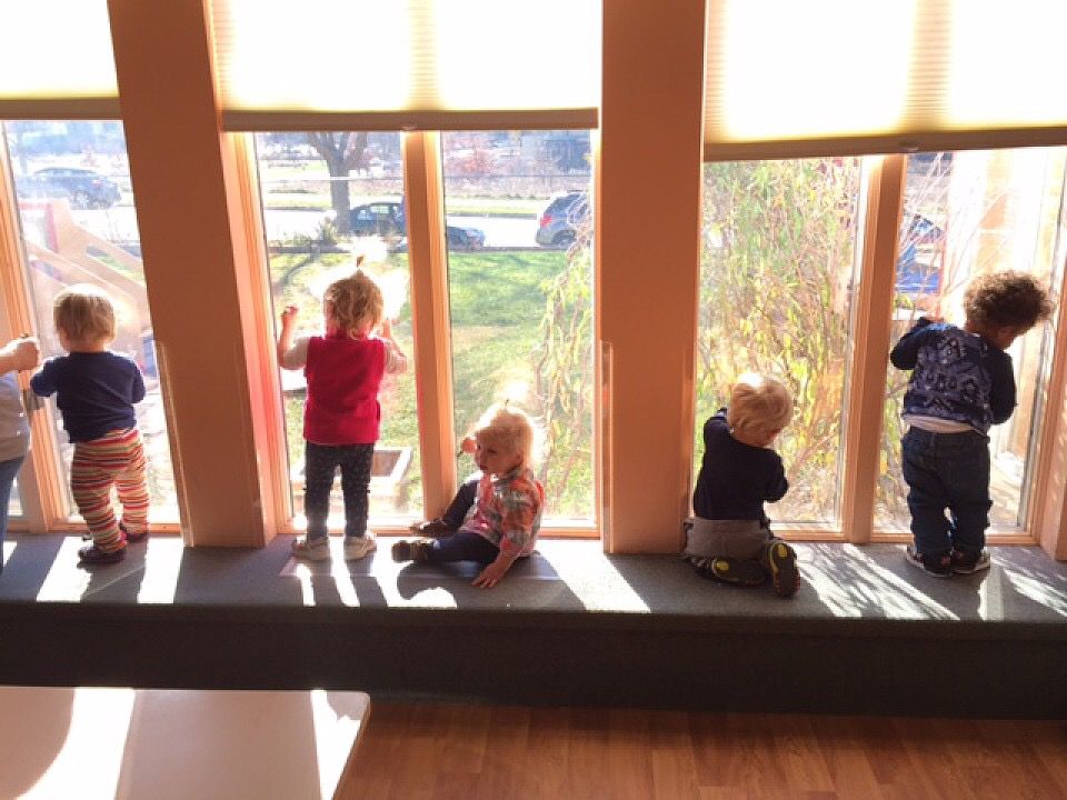 Toddlers stand on a bench looking out the windows of the center.