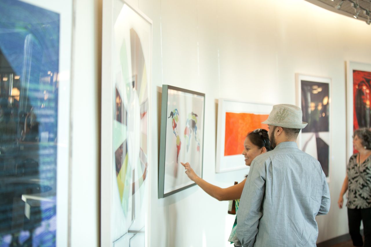 Two people point out what they are observing on a painting hanging in the BTC.