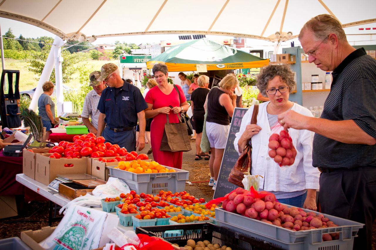 The Farmer's Market with booths of flowers, fresh produce and people.