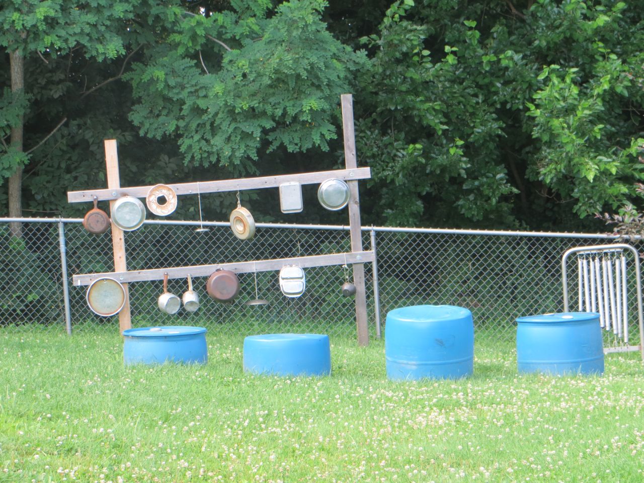 Pots and pans hang from wooden beams with blue barrels of different sizes to mark where children can have outdoor music time.