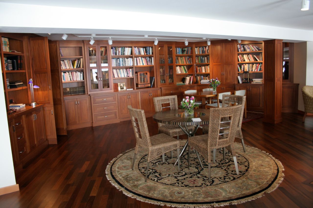 The interior of the Earth House that includes a wall full of books on shelves and a circular rug with table and chairs in the middle of the room.