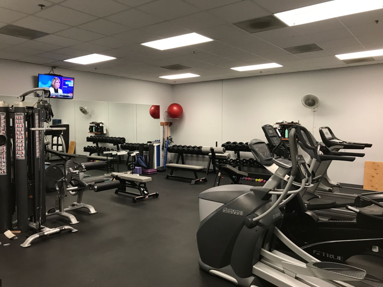 The workout room of the BTC which includes floor to ceiling mirrors, treadmills, free weights, machines and a mounted television.