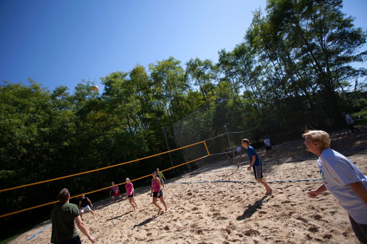 Two teams play volleyball under a high noon sun.