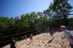 Two teams play volleyball under a high noon sun.