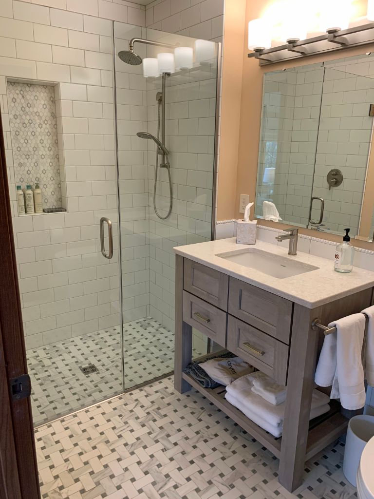 a bathroom with a white tiled shower with glass doors, a small vanity with a mirror above