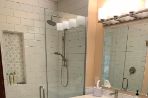 a bathroom with a white tiled shower with glass doors, a small vanity with a mirror above