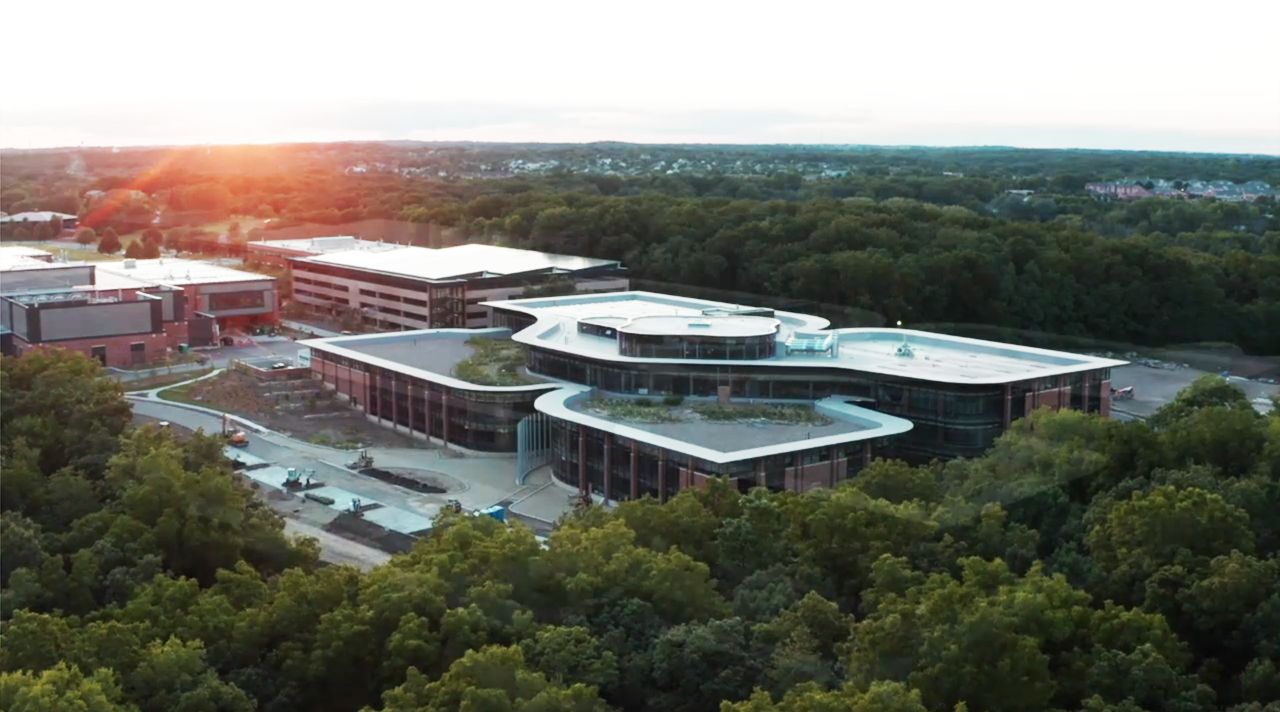 a drone shot of the four leaf clover shaped building, where the sun is just rising over the trees