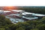 a drone shot of the four leaf clover shaped building, where the sun is just rising over the trees