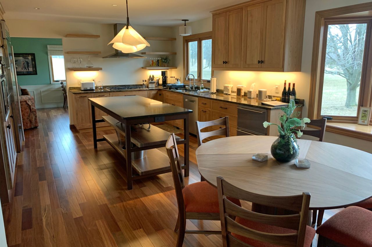 a kitchen with wood flooring, open shelving, an island, and a round dinner table