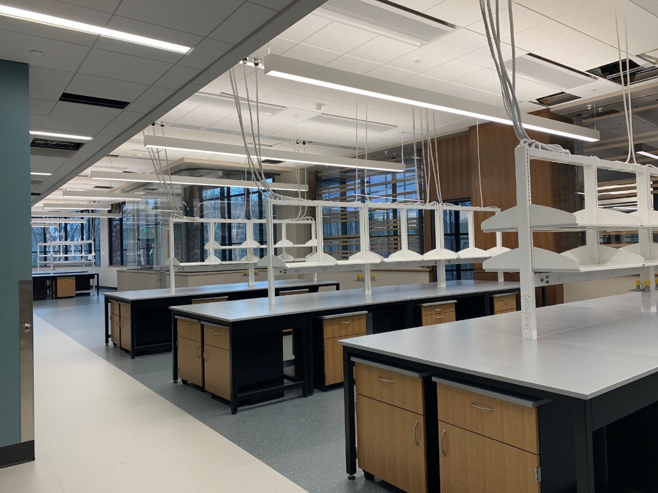 lab benches in a long room with white counter tops, black and wooden cabinets, and white shelving