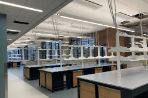 lab benches in a long room with white counter tops, black and wooden cabinets, and white shelving