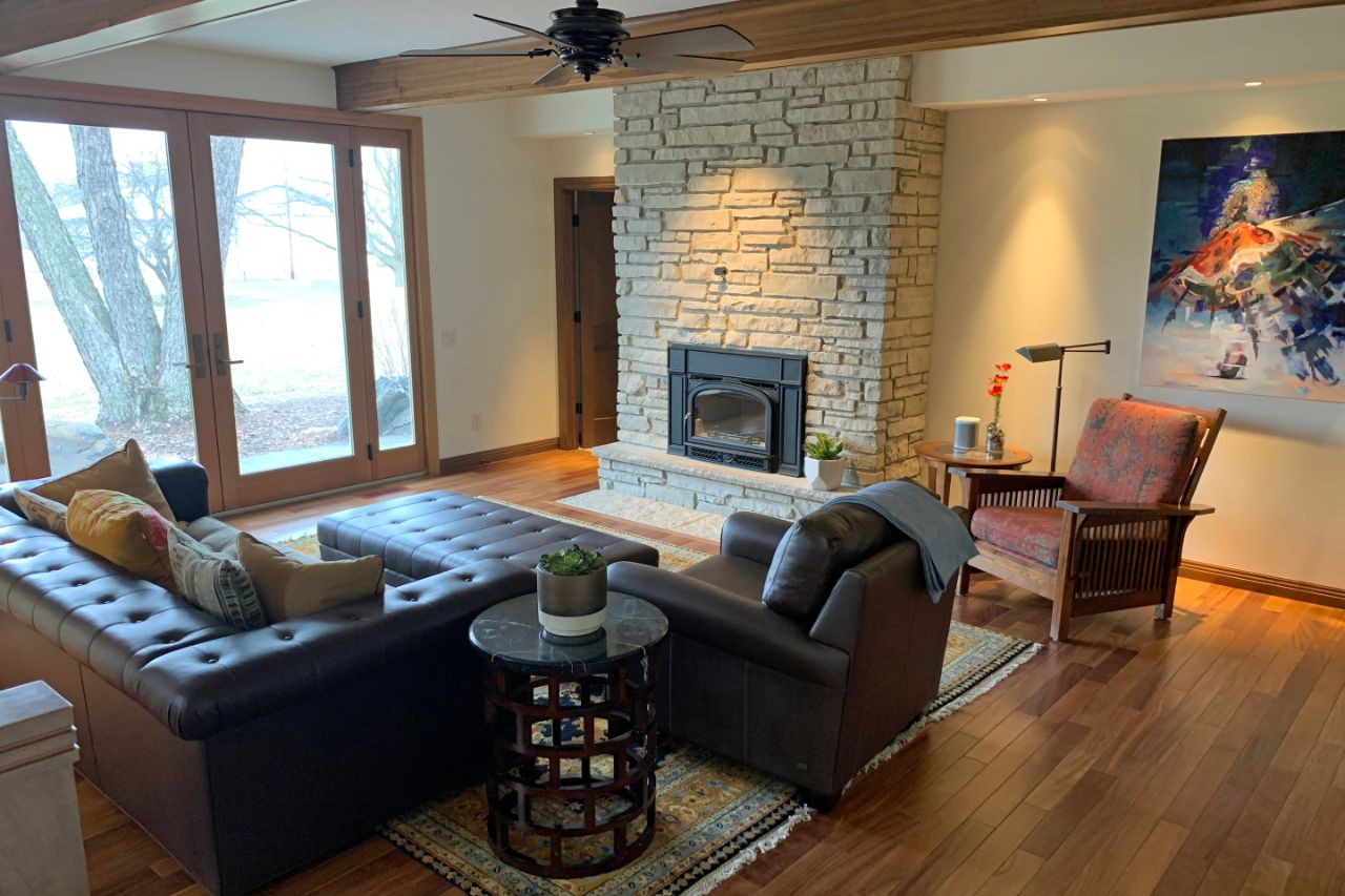 this is a hard wood floor room with a fireplace on the right wall and a leather couch and chair facing the fireplace with a leather ottoman. On the far wall are floor to ceiling glass sliding doors.