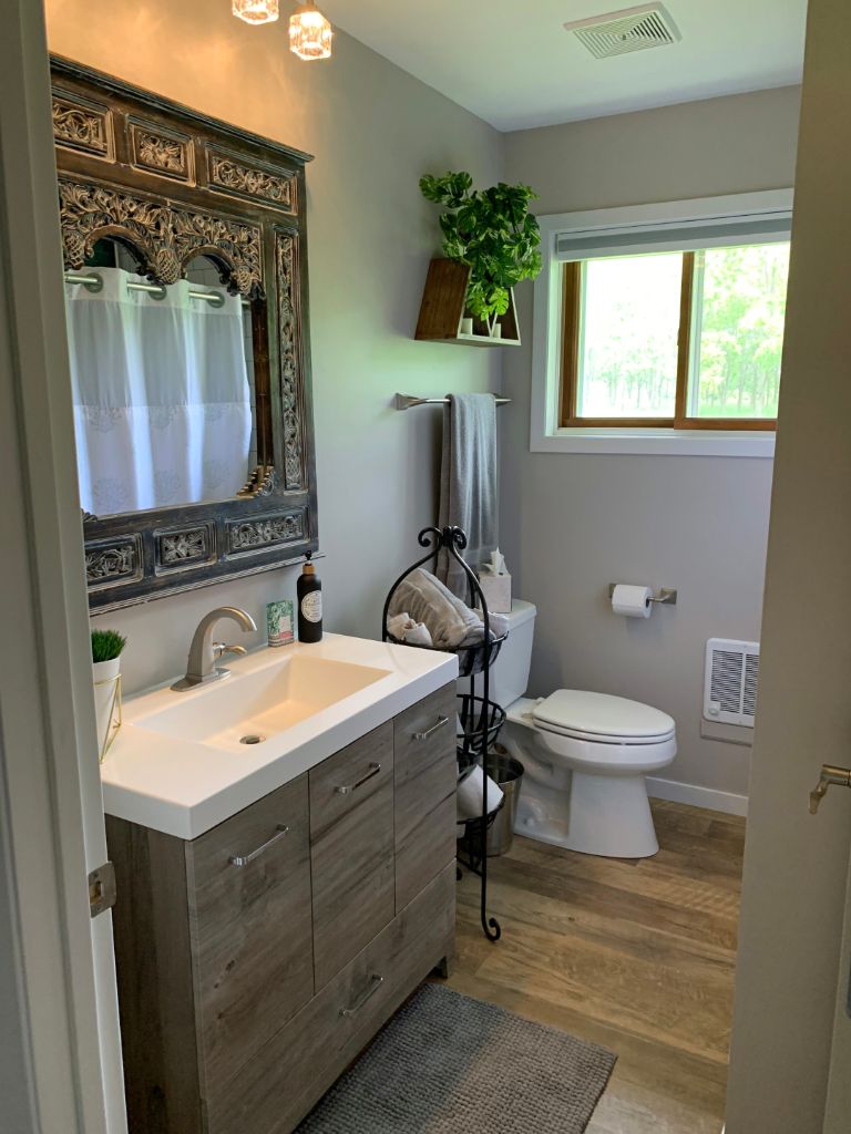 bathroom with small vanity and mirror, wood floors and toilet in the corner