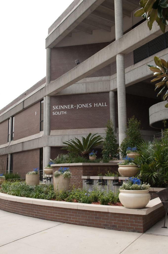 Red brick building with white columns and trim with a fountain and shrubbery in front