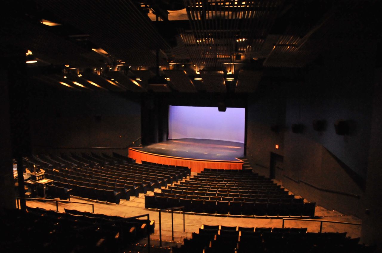 Large, black-walled auditorium with theater-style seating and a wide stage with a blue background.