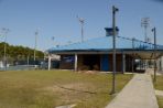 Square one-story brick building with white columns and blue doors and blue metal roof; to the left of the building are tennis courts where student athletes are practicing.