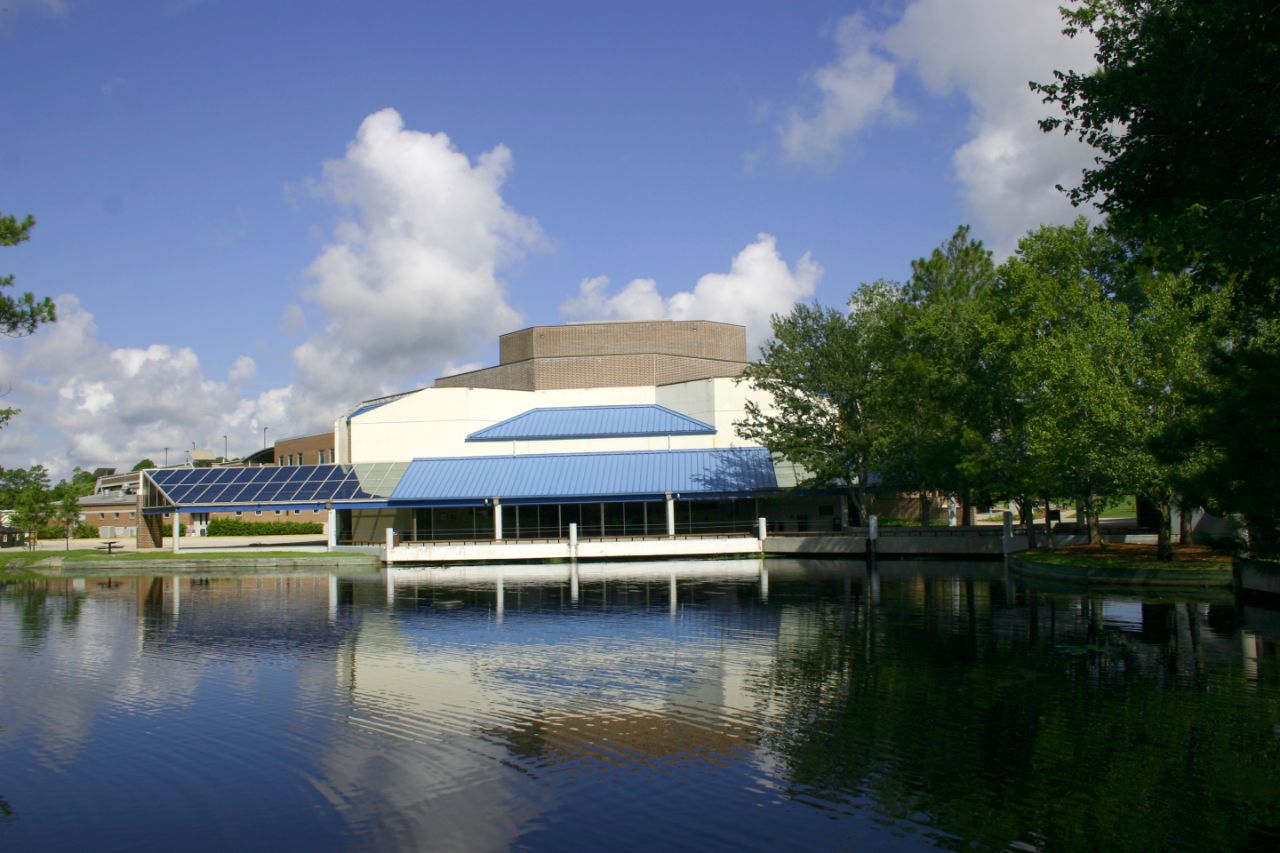 White one-story building with a blue awning located in front of a lake with trees to the right.