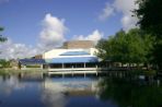 White one-story building with a blue awning located in front of a lake with trees to the right.