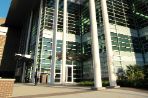 Tall steel and glass building with large columns and broad metal awning with palmetto plants and a brick walkway in front