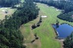 Aerial view of golf course with two sand traps near a putting area and a lake in the distance, surrounded by dense trees.