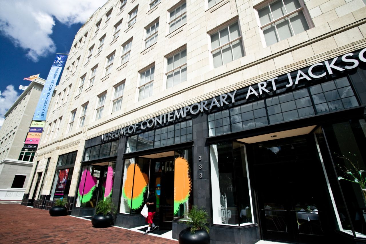 Five-story building in an urban setting with black slate tile façade across the first level and brightly colored entrance featuring the words Museum of Contemporary Art Jacksonville above the entryway.