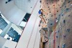 A student wearing a harness and helmet makes his way up the rock climbing wall that sits inside a three-story atrium.