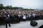 Photo taken from stage looking into a large crowd of students who are packed on the lawn; Ozzie Osprey mascot character is standing in front of the security fence near the stage posing in front of the crowd.