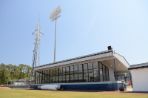 One-story building with white trim and floor to ceiling glass windows sits along the first base line with the stadium lights in the background.