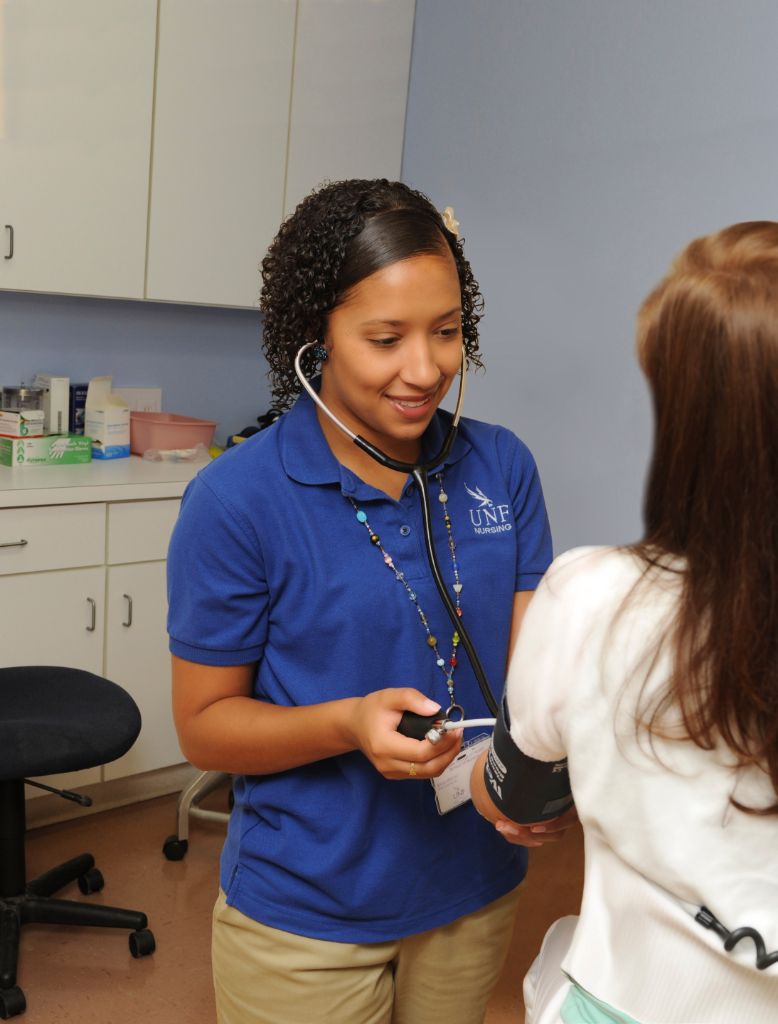 A female nursing student is taking the blood pressure of a female patient in a doctor's office.